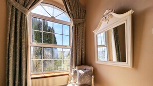 A room with a large window, a radiator, a chair, and a mirror on the wall.