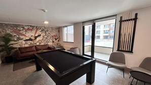 Une table de billard dans une pièce comprenant un canapé, des fauteuils et une grande fenêtre.