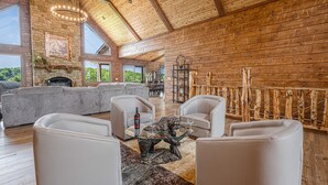 Amplia sala de estar con chimenea de piedra, sofás de cuero blanco y una mesa de centro de vidrio.