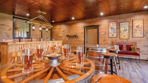 Una zona de bar rústica con decoración de madera, una gran mesa en forma de rueda de madera y carteles antiguos en la pared.