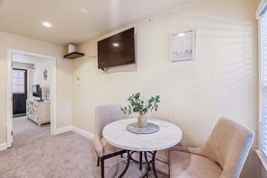 A dining area with a round table, two chairs, a vase with flowers, a flat-screen TV mounted on the wall, and a framed picture.
