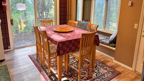 Een eetruimte met een tafel voor vier personen, houten stoelen, een rode tafelkleed en uitzicht op de omgeving door grote ramen.