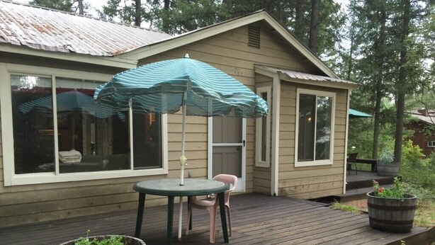 Een houten terras met een tafel, stoelen, een gestreepte parasol en potplanten.