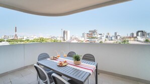 Un balcón con una mesa para dos, vistas de la ciudad, una planta y una botella de jugo de naranja.