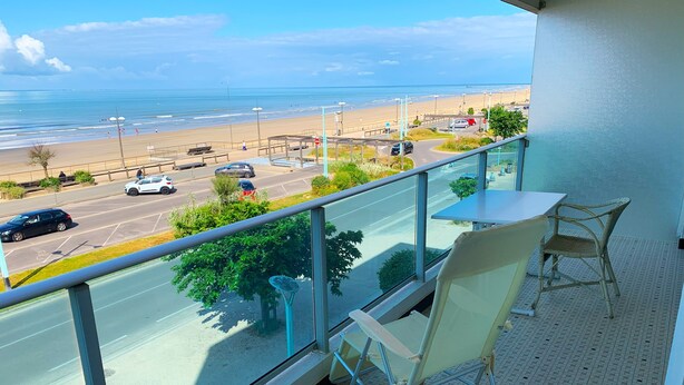 Un balcon avec vue sur la plage et la route. On y trouve deux chaises et une table.