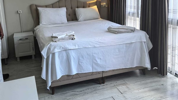 A hotel room with a large bed, a bedside table, a nightstand, an air conditioning unit, and a window with curtains. - Old City Pansiyon (Istanbul)
