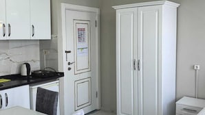 A compact kitchen with white cabinets, a countertop with a kettle, and a door with a notice. - Old City Pansiyon (Istanbul)