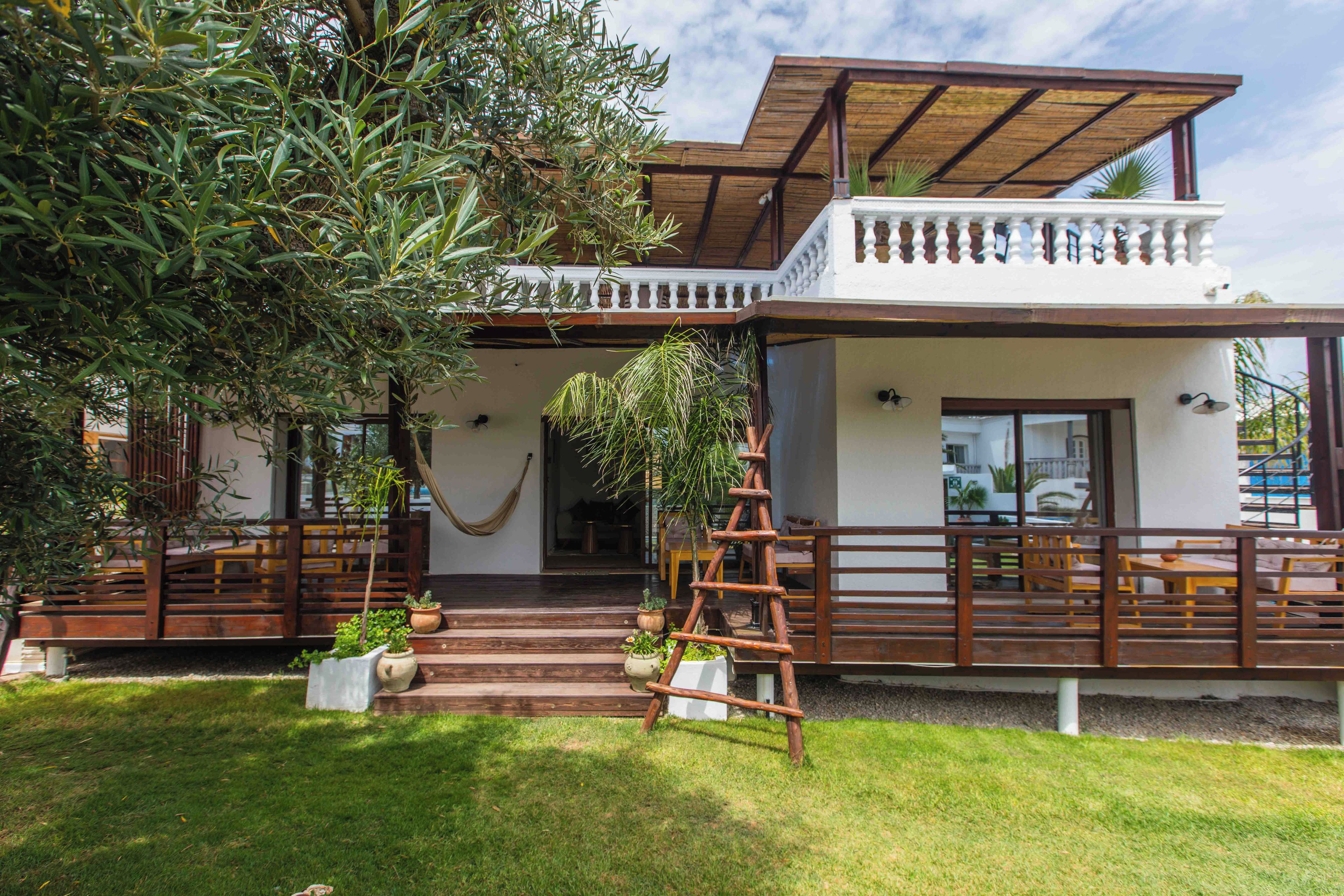 A two-story house with a wooden deck, a hammock, and a staircase leading to the upper level.