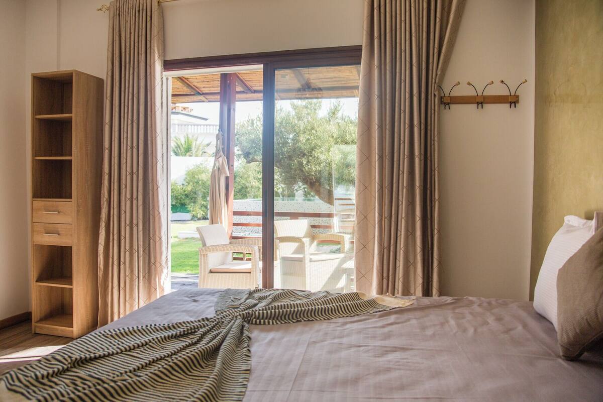 A bedroom with a bed, a wooden wardrobe, and a view of an outdoor patio with chairs and a table.