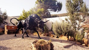 A sculpture of a mechanical bull in a garden with a bench, trees, and cacti. - Dar Lina  (El Haouaria)