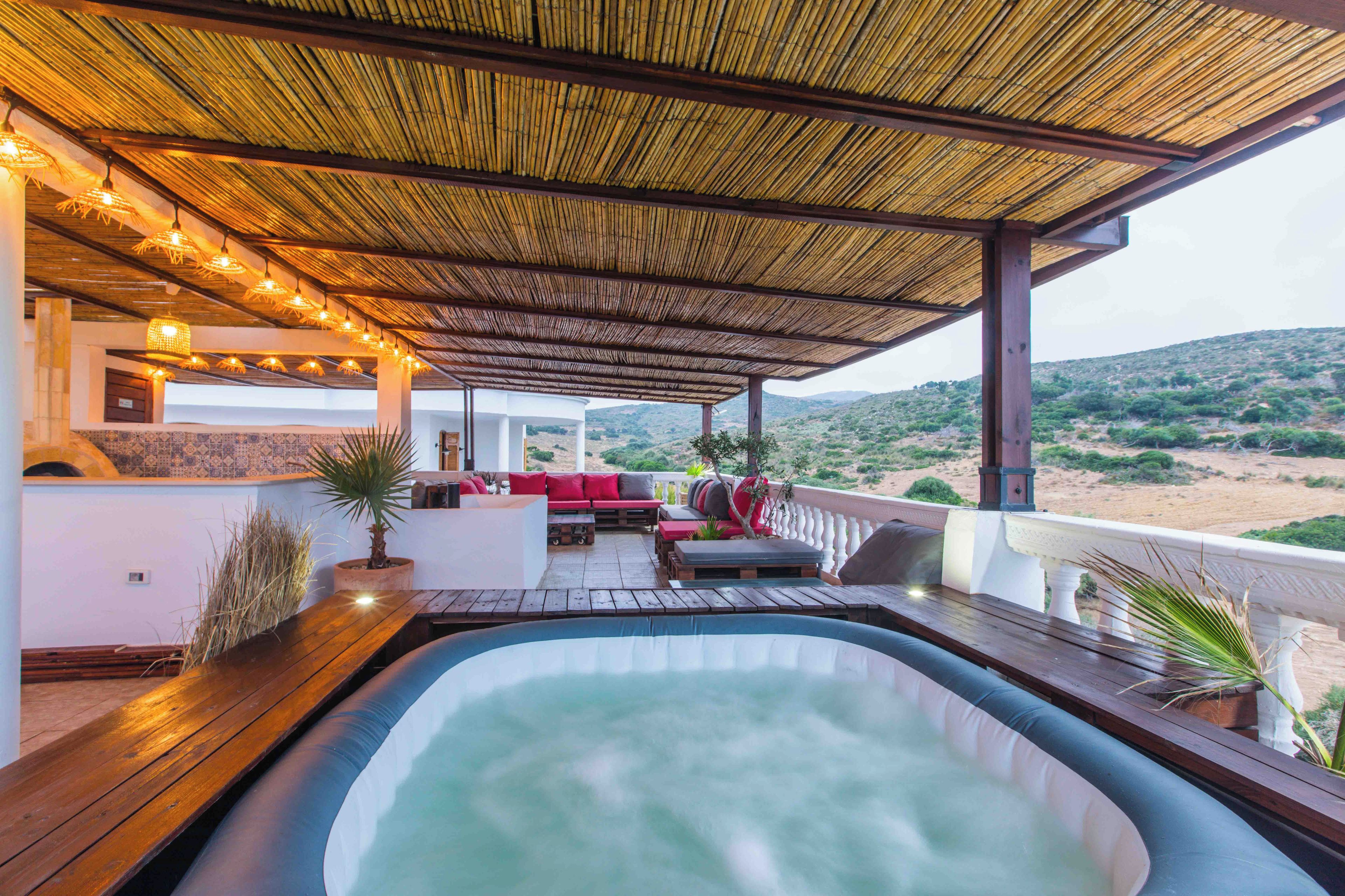 A hot tub area with a wooden deck, seating, and a view of the landscape.
