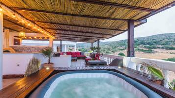 A hot tub area with a wooden deck, seating, and a view of the landscape.