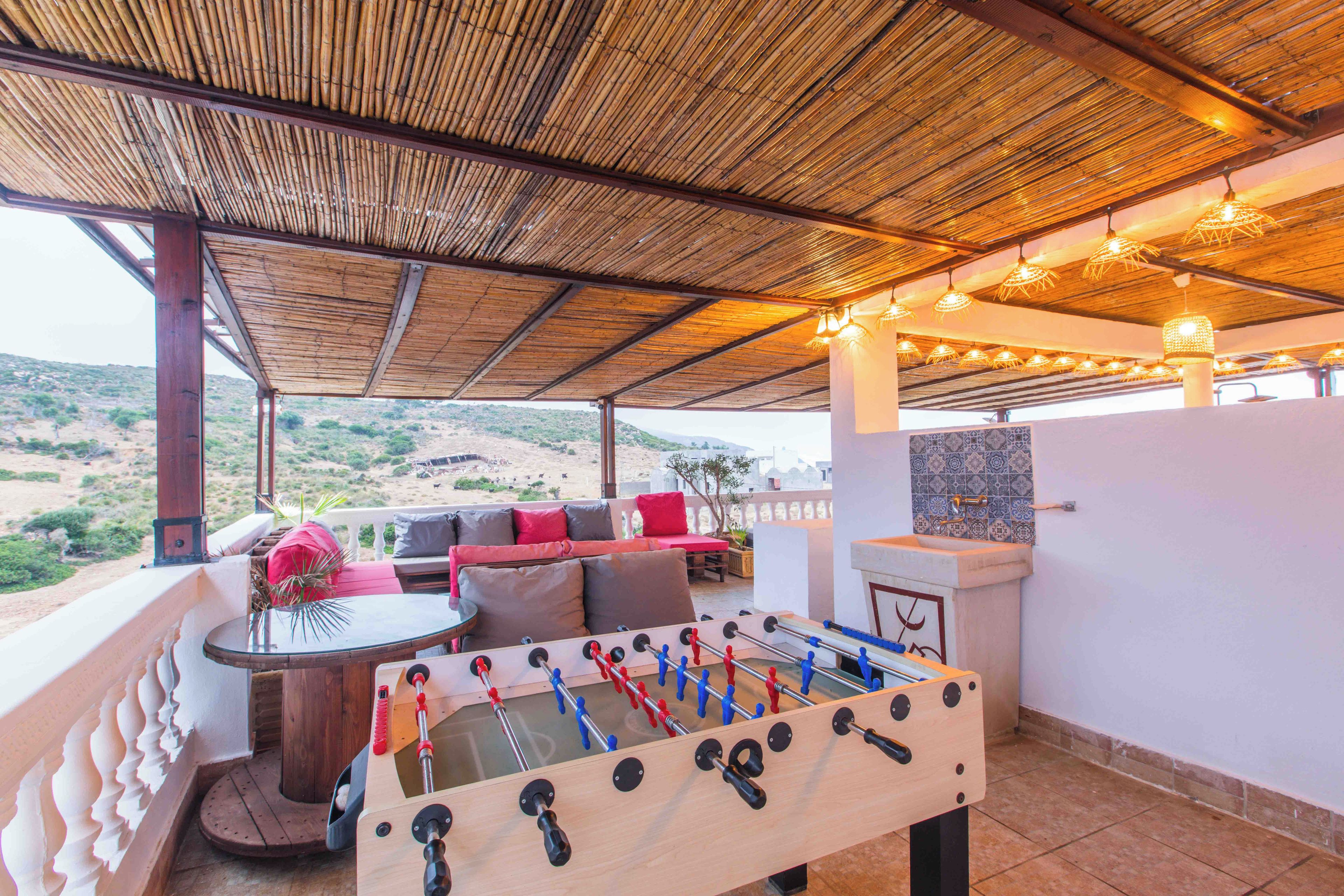 An outdoor seating area with a foosball table, a sofa with cushions, and a view of the landscape.