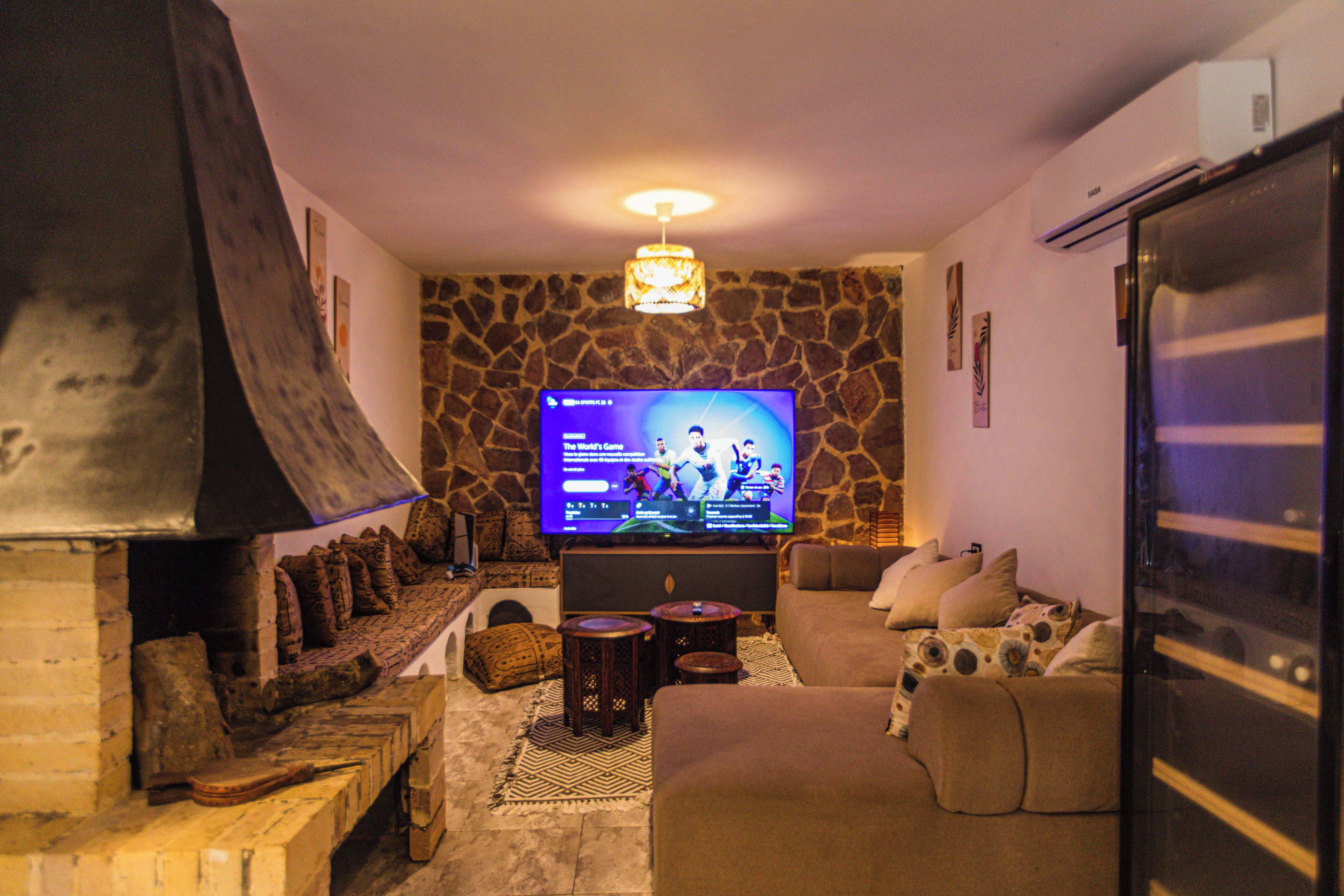 Una sala de estar con pared de piedra, chimenea, televisor y sofá.