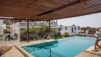 Une piscine sur le toit, dotée d’une terrasse en bois, d’un espace salon couvert et offrant une vue sur le paysage urbain.