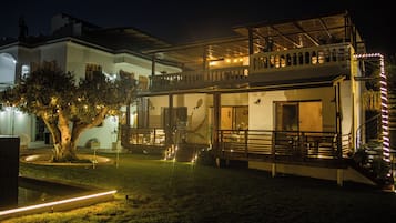 Une maison à deux étages avec un balcon, un arbre dans la cour et des guirlandes lumineuses.