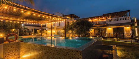 A swimming pool with a tiled edge, surrounded by a covered patio area with string lights.