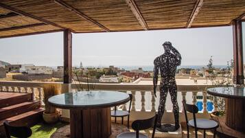 Um pátio externo com mesa de vidro, cadeiras e uma estátua.