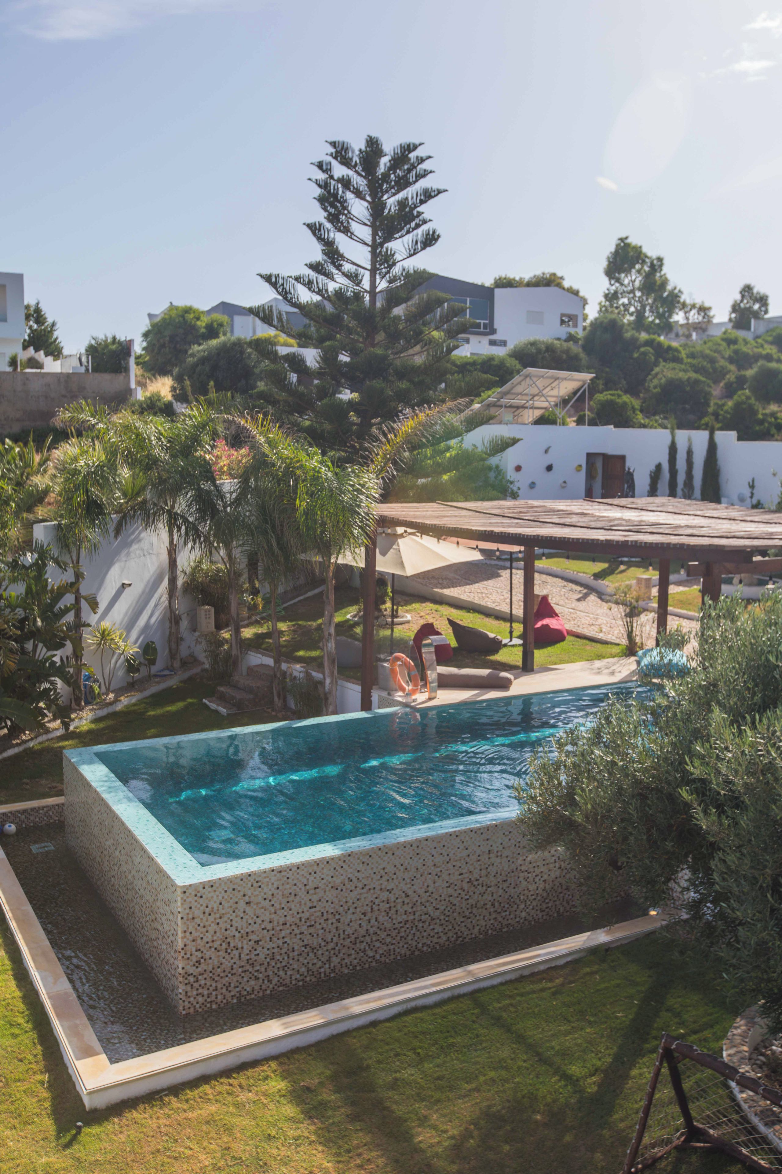 Una piscina rectangular con borde de azulejos, rodeada de césped y una terraza de madera.