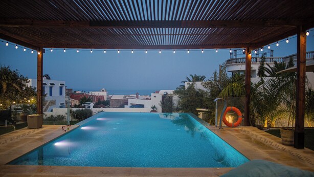A swimming pool with a view of the sea, surrounded by a wooden pergola and string lights. - Dar Lina  (El Haouaria)