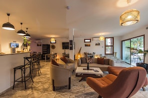 Un salon moderne comprenant un canapé, des fauteuils, une table basse et un coin repas avec des tabourets de bar.