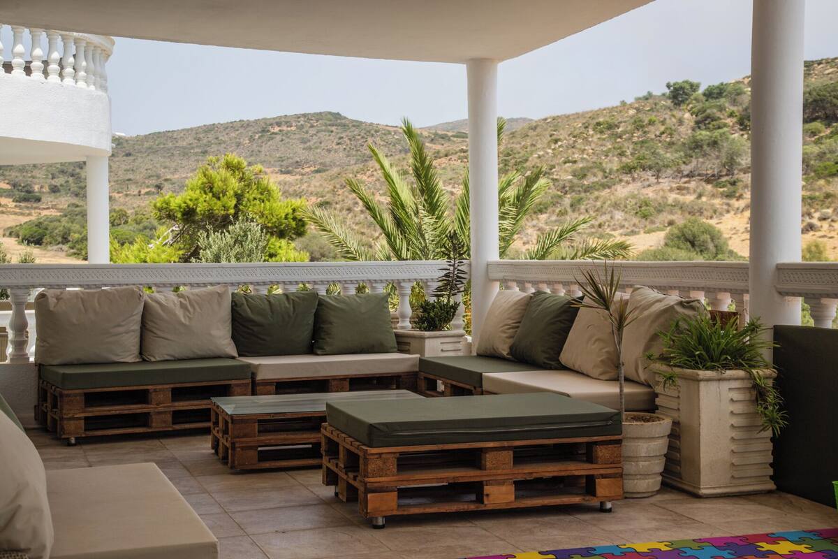 A covered outdoor seating area with a view of a hilly landscape.