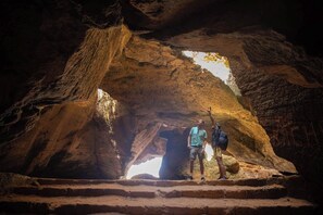 A person standing at the entrance of a cave with a large rock archway. - Dar Lina  (El Haouaria)