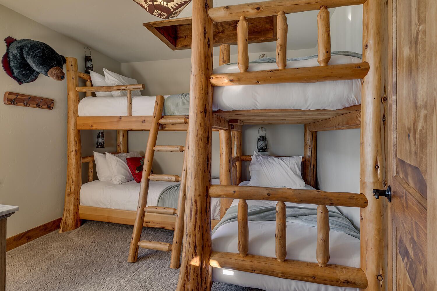 A bunk bed room with wooden railings, a ladder, and a bear decoration on the wall.