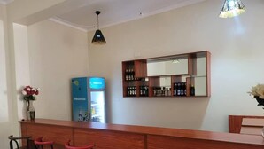 Zona de bar con mostrador de madera, tres taburetes rojos, un mini bar y un espejo sobre el mostrador.