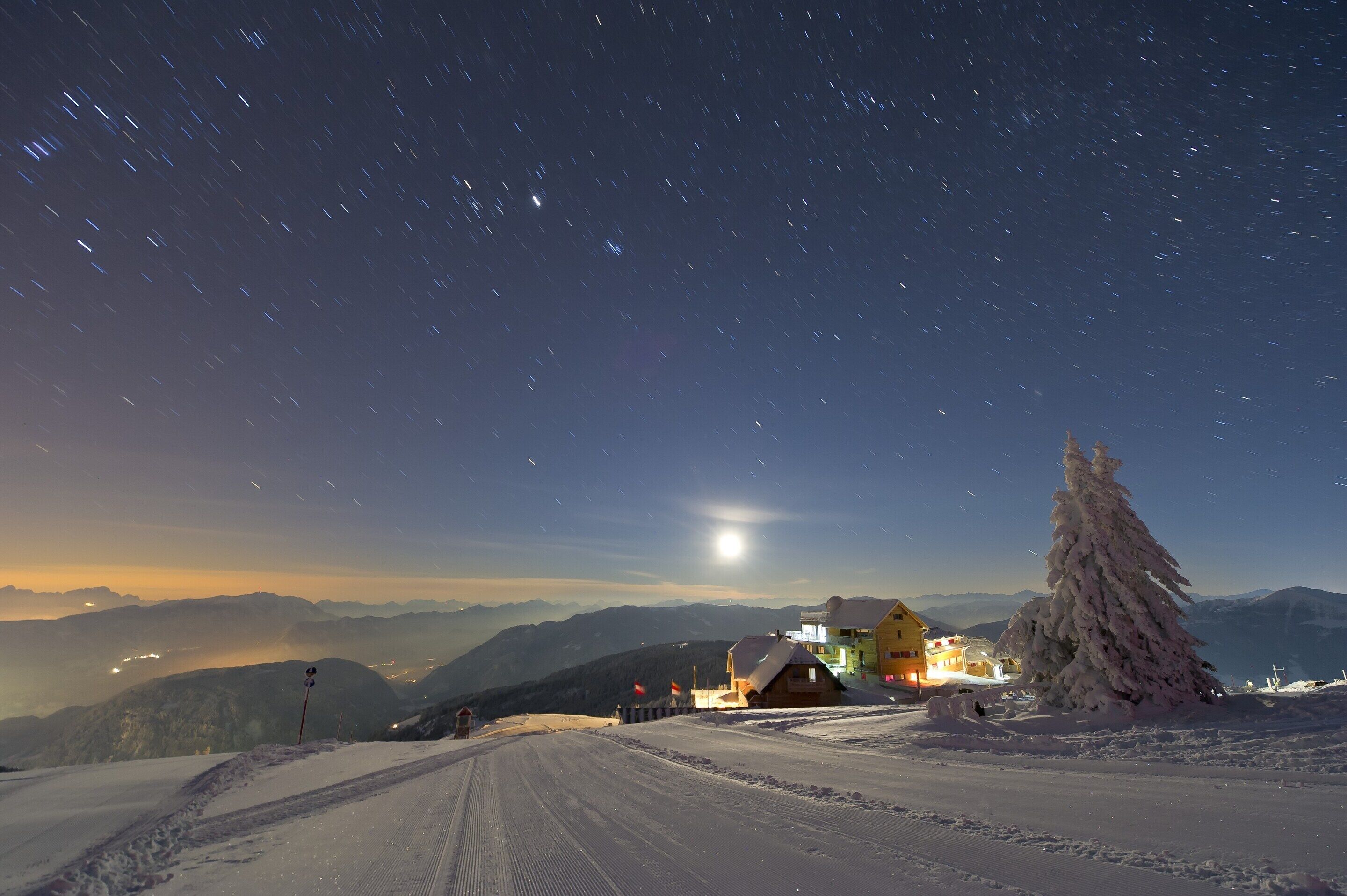 Eine verschneite Landschaft mit einem Gebäude und einem mit Schnee beladenen Baum.