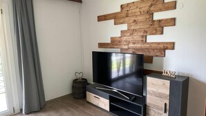 En moderne stue med et fladskærms-TV, trædekoration på væggen og et skab med et 'LOVE'-skilt.