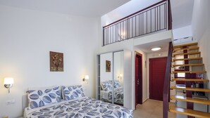 Ein Schlafzimmer mit Bett, Kleiderschrank, Spiegel, Treppe und einer roten Tür.