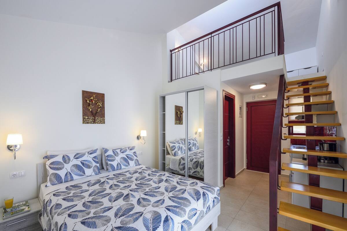 Ein Schlafzimmer mit Bett, Kleiderschrank, Spiegel, Treppe und einer roten Tür.