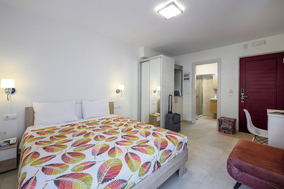 A hotel room with a bed, bedside tables, a desk, a chair, a wardrobe, and a bathroom.
