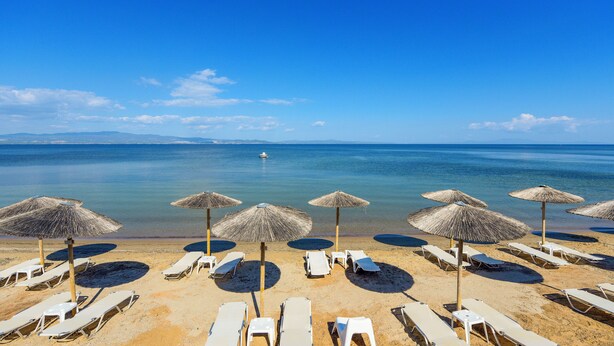 Ein Strand mit Liegestühlen und Reetdachsonnenuren, klares blaues Meer und ein Boot in der Ferne.