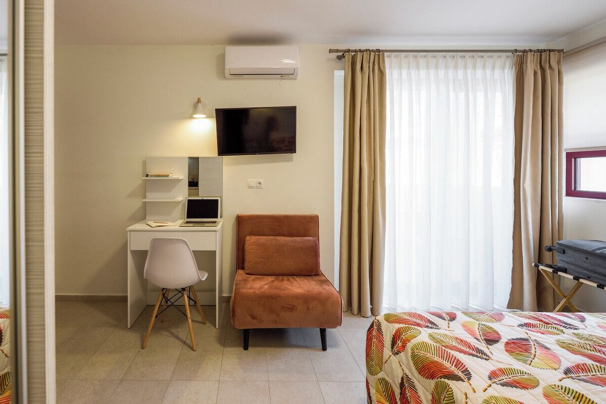 A hotel room with a desk, chair, two beds, a TV, and curtains.