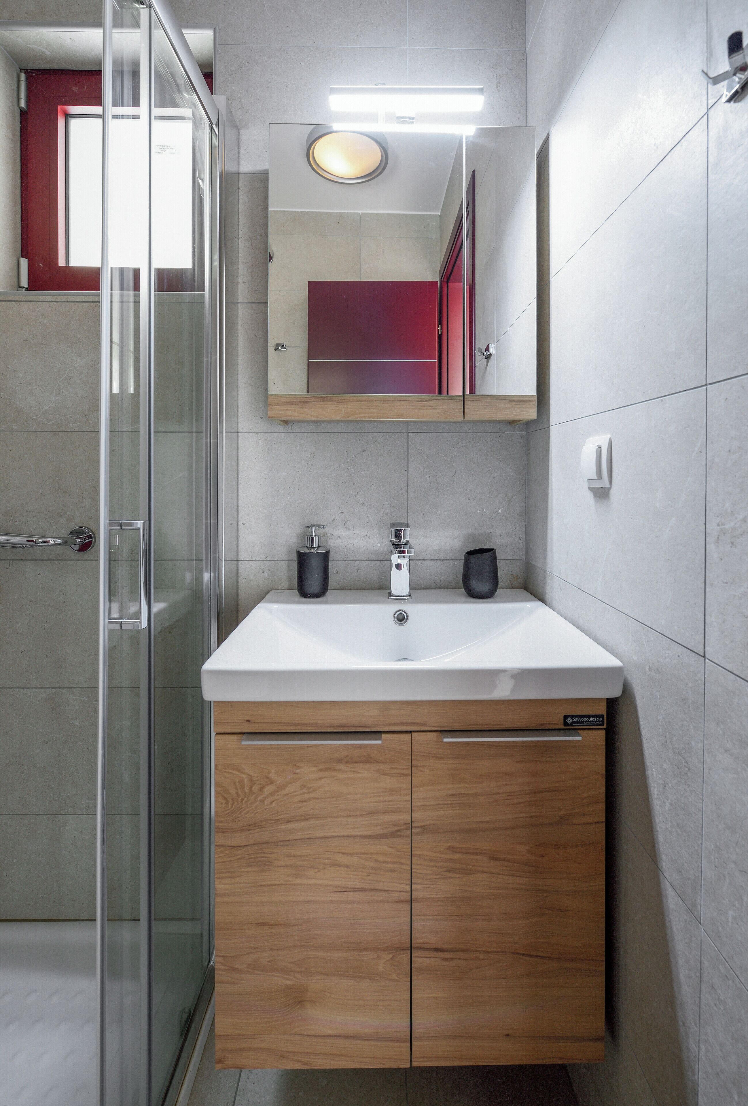 A modern bathroom with a glass shower enclosure, a white sink with a wooden vanity, and a mirror above the sink.