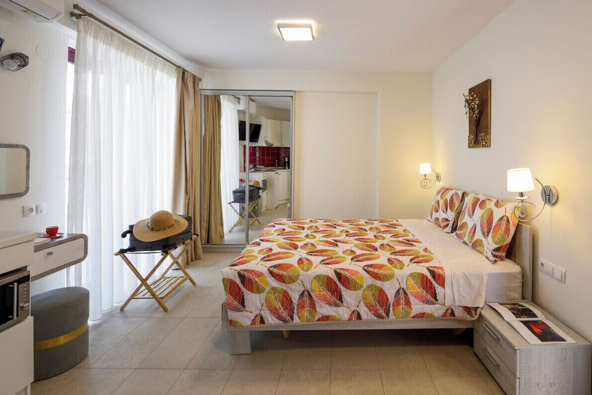 A bedroom with a bed, bedside tables, a desk, a chair, a mirror, and a wardrobe.