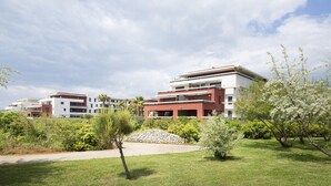 Un immeuble résidentiel moderne doté de nombreux balcons, entouré de jardins bien entretenus et surplombant un ciel dégagé.