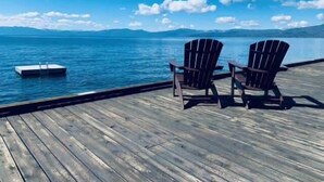 A wooden deck with two Adirondack chairs facing a body of water and distant mountains. - Million Dollar Views of Lake Tahoe - #13 (Kings Beach)