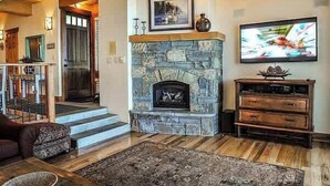 A living room with a stone fireplace, a television, and a staircase leading to another room. - Serene Lakefront Townhouse with Breathtaking Views at Brockway Springs- #4 (Kings Beach)