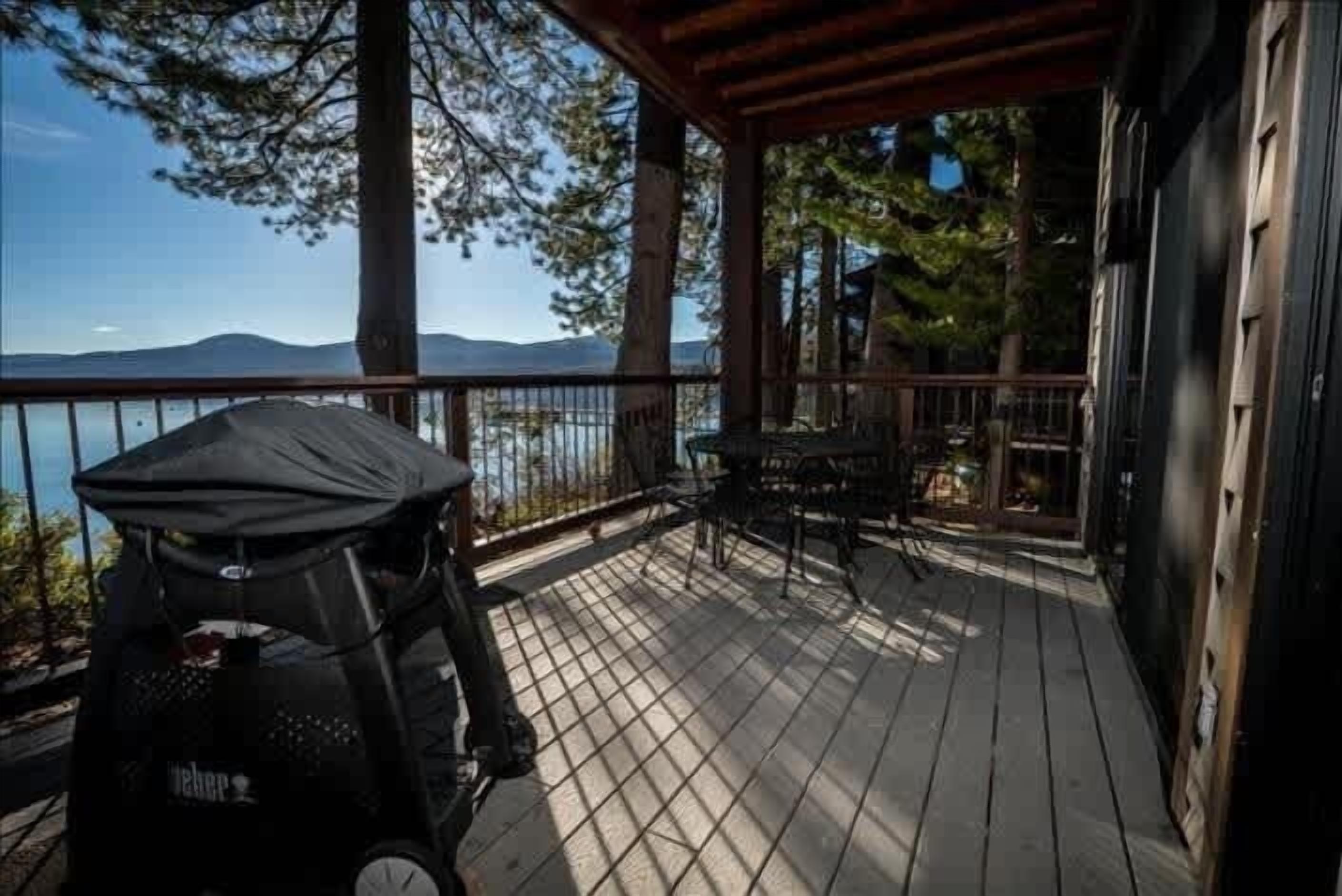 A wooden deck with a covered seating area, overlooking a body of water and mountains.
