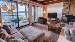 A spacious living room with a large TV, comfortable seating, and a stone fireplace. - Original Charm with Stunning Lake Tahoe Views-#6 (Kings Beach)