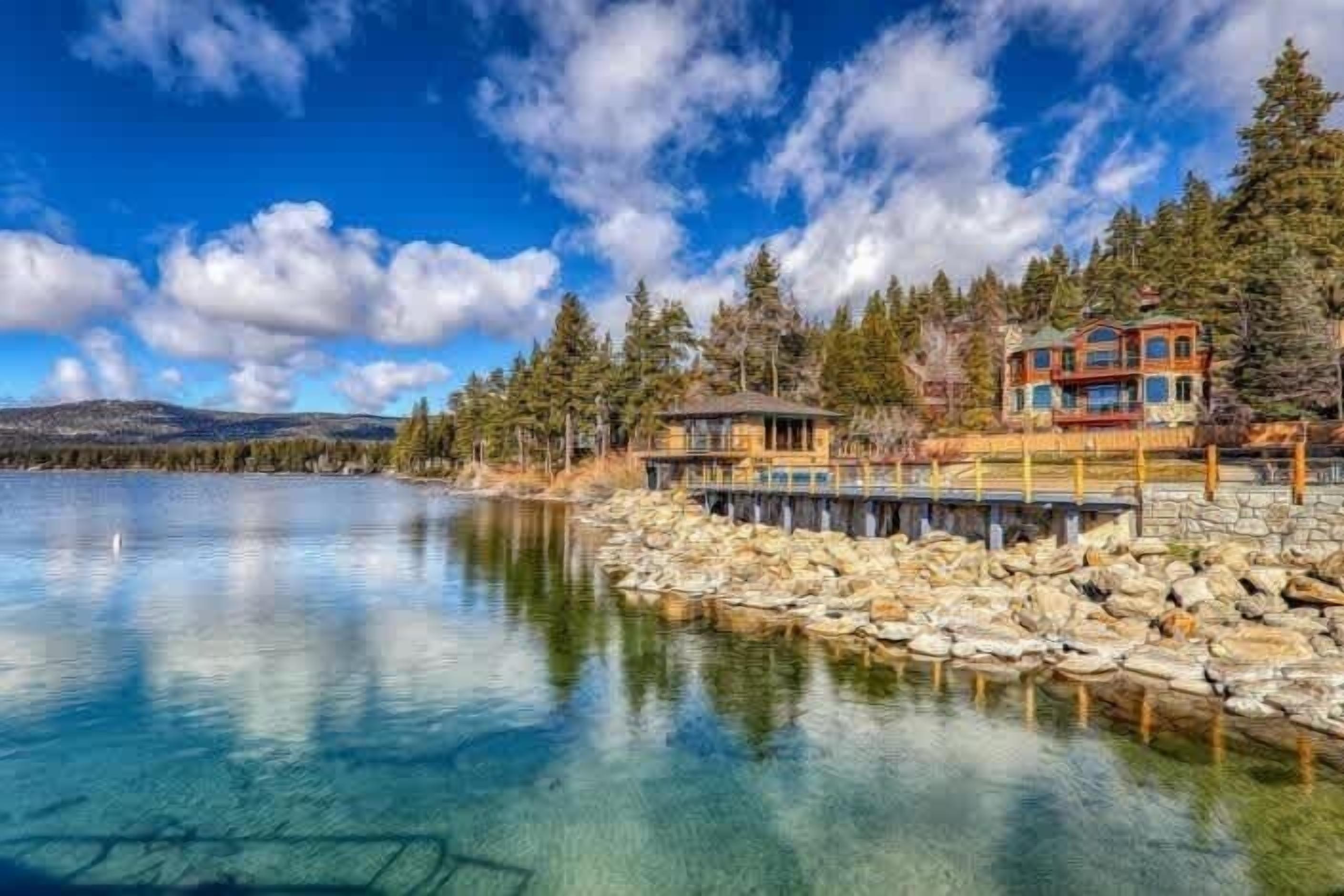 A lakeside property with a stone dock, a wooden cabin, and a multi-story building with a red roof.