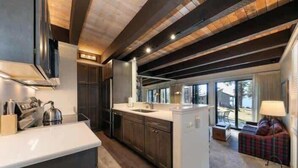 A modern kitchen with dark wood cabinets, a white countertop, and a built-in island. There is a large window providing natural light and a view of the outdoors. - Newly Remodeled Lake-View retreat #21 (Kings Beach)