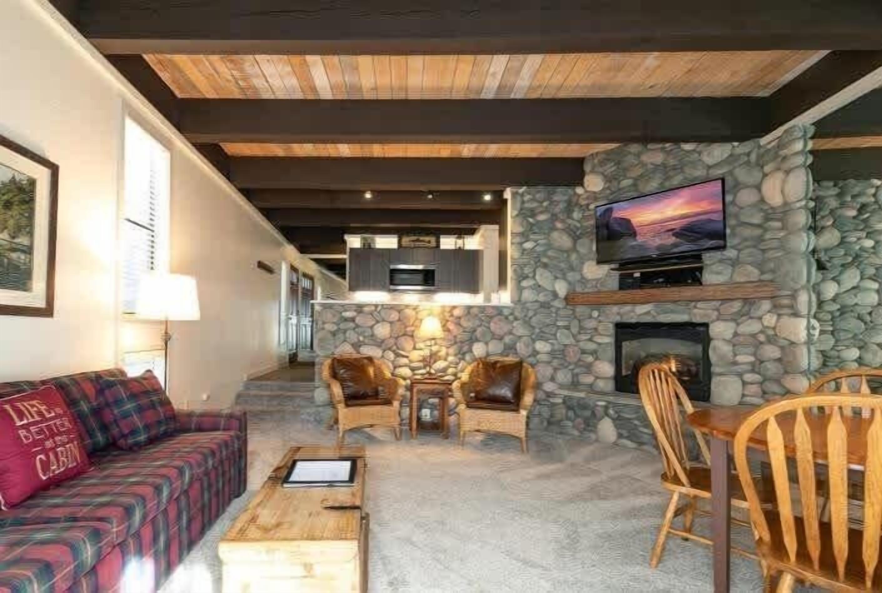 Un salon chaleureux avec une cheminée en pierre, un téléviseur fixé au mur et un coin salon confortable comprenant un canapé et des fauteuils.