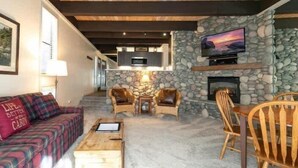 A cozy living area with a stone fireplace, a television mounted on the wall, and a comfortable seating arrangement including a sofa and chairs. - Newly Remodeled Lake-View retreat #21 (Kings Beach)