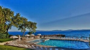 A pool area with a view of the sea and mountains, surrounded by greenery and umbrellas. - Lakefront Condo in Kings Beach-#37 (Kings Beach)