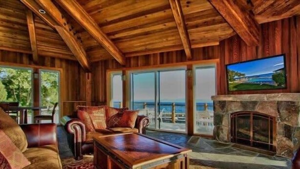 A wooden interior with a stone fireplace, leather furniture, and large windows overlooking a scenic view. - Lakefront Condo in Kings Beach-#37 (Kings Beach)