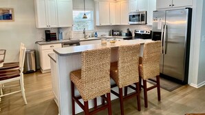 A modern kitchen with white cabinets, stainless steel appliances, and a central island with wicker bar stools.